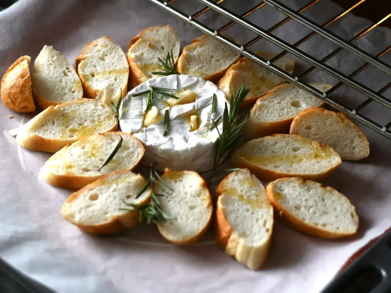Pyszny, pieczony camembert z czosnkiem i rozmarynem, otoczony kromkami bagietki. Idealna przekąska na ciepło.