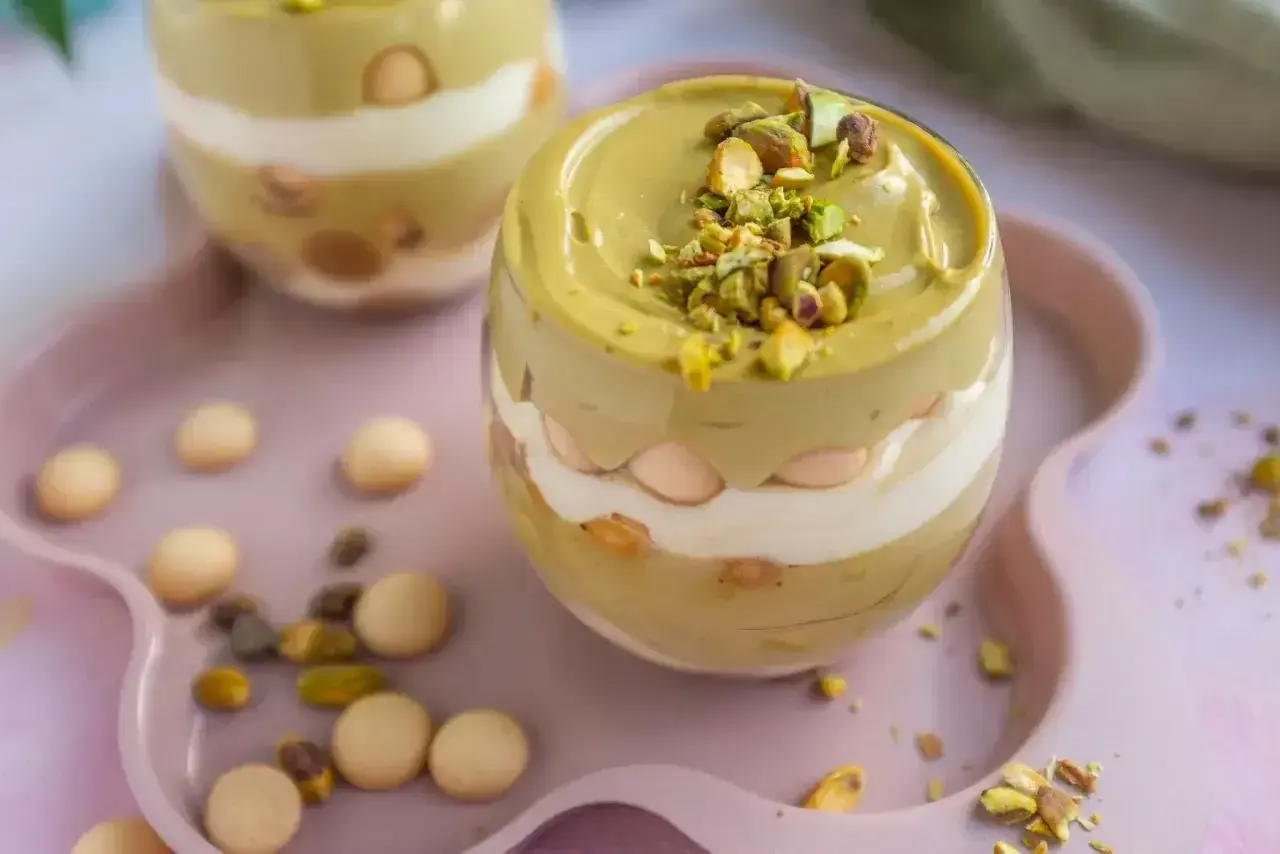 Pyszny deser w pucharku: krem pistacjowy z mascarpone, przełożony biszkoptami i posypany orzechami.