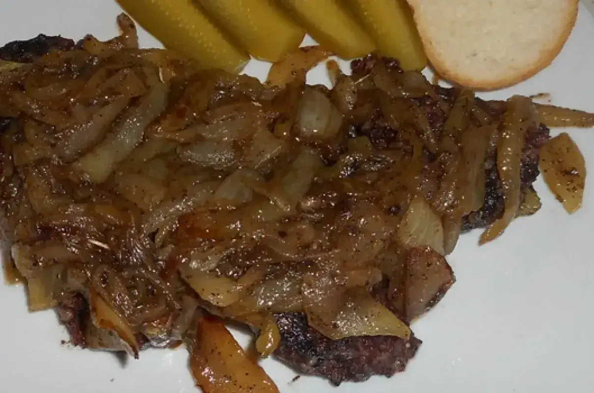 Pyszna kaszanka z patelni, duszona z cebulką, podana z ogórkiem kiszonym i kromką chleba.
