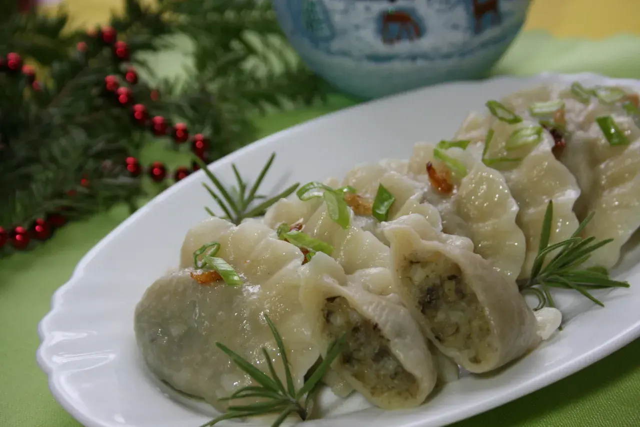 Pyszne, domowe pierogi ukraińskie, udekorowane szczypiorkiem i rozmarynem, prezentują się apetycznie na białym talerzu.