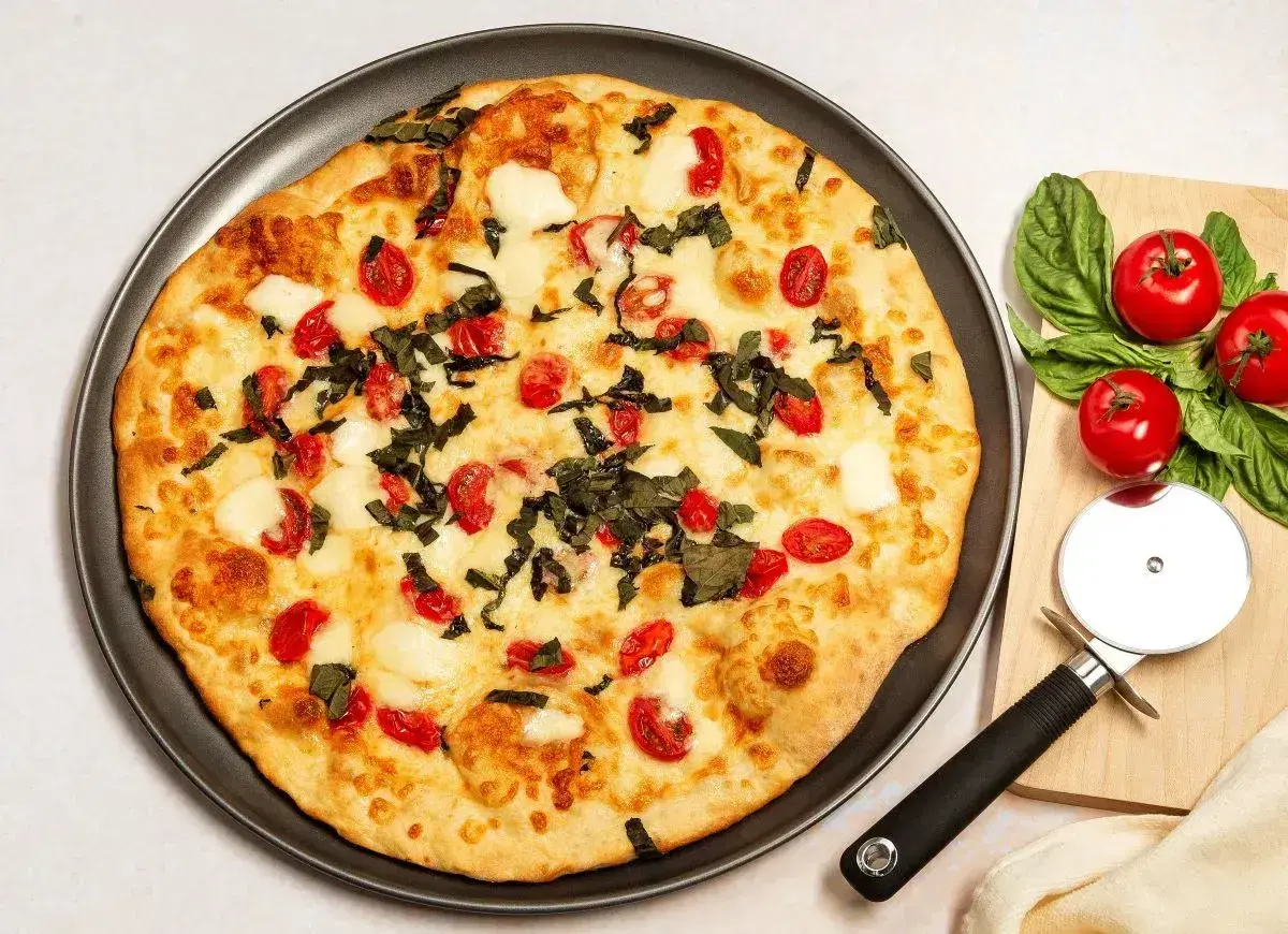 Pyszna pizza z serka wiejskiego, pomidorkami koktajlowymi i bazylią. Obok leży nóż do pizzy i świeże pomidory.