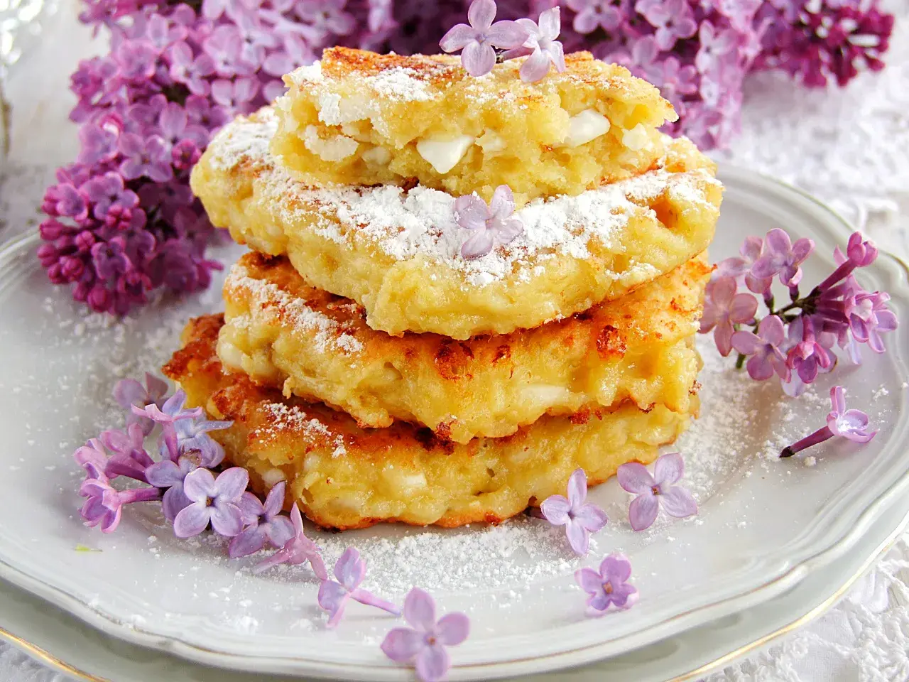 Fit placuszki z serka wiejskiego i banana, posypane cukrem pudrem, ozdobione fioletowymi kwiatami bzu.