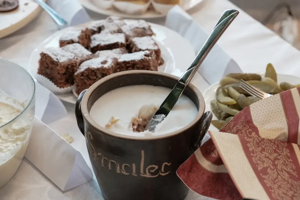Gęsty smalec w glinianym naczyniu, obok ciasto czekoladowe i ogórki.