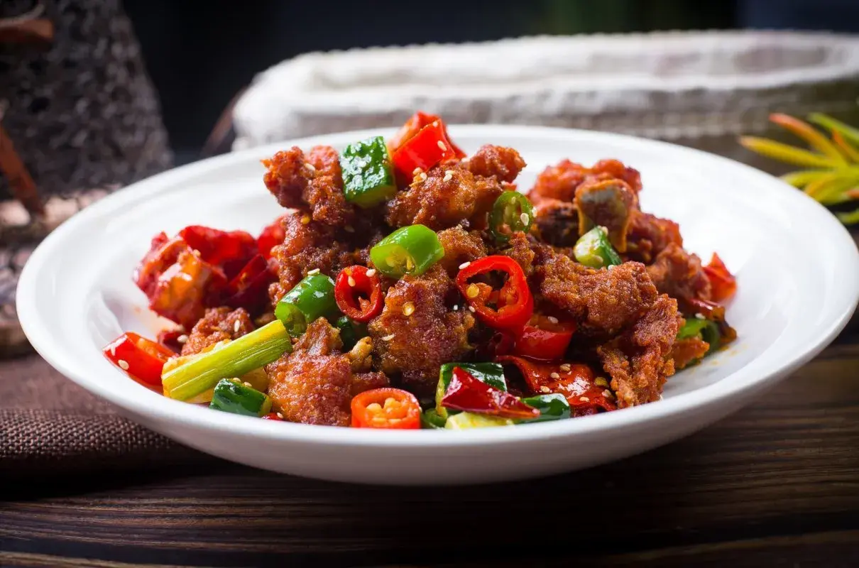 Chrupiący kurczak po kantońsku z papryczkami chili i zieloną cebulką na białym talerzu.