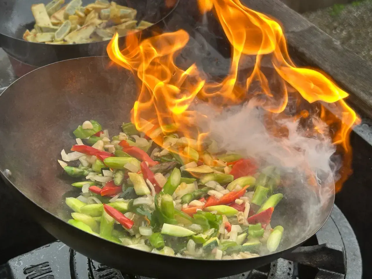 Ogień buchający z woka podczas przygotowywania pysznego stir fry z warzywami.