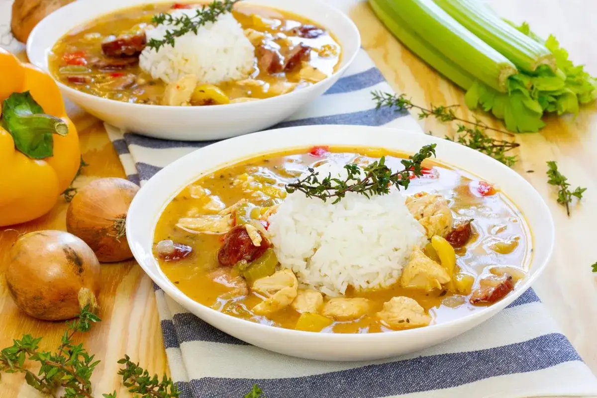 Dwie miski aromatycznego gumbo z kurczakiem, kiełbasą i ryżem, obok papryki, cebuli i selera.