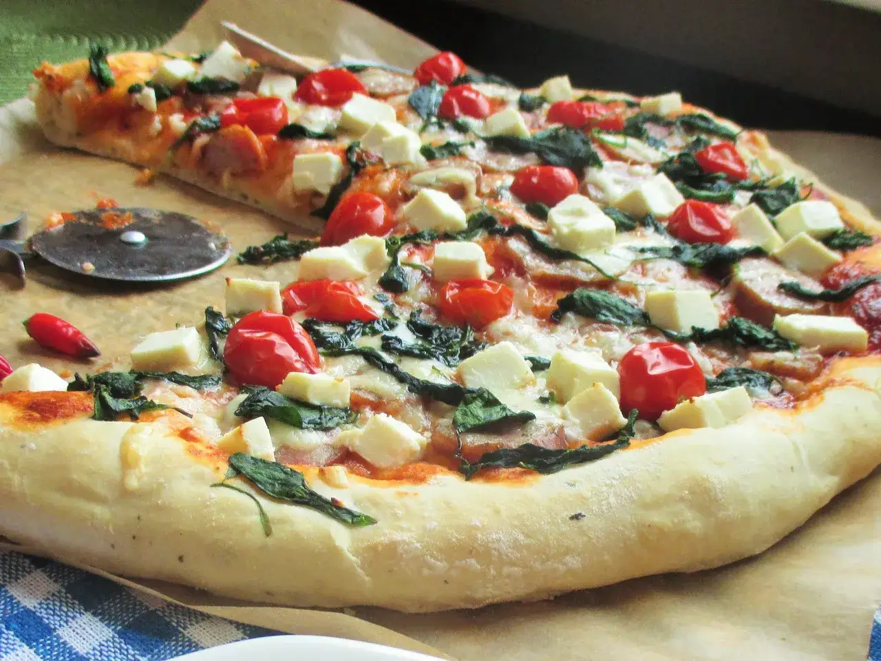 Pyszna pizza ze szpinakiem, pomidorkami i fetą, gotowa do pokrojenia.