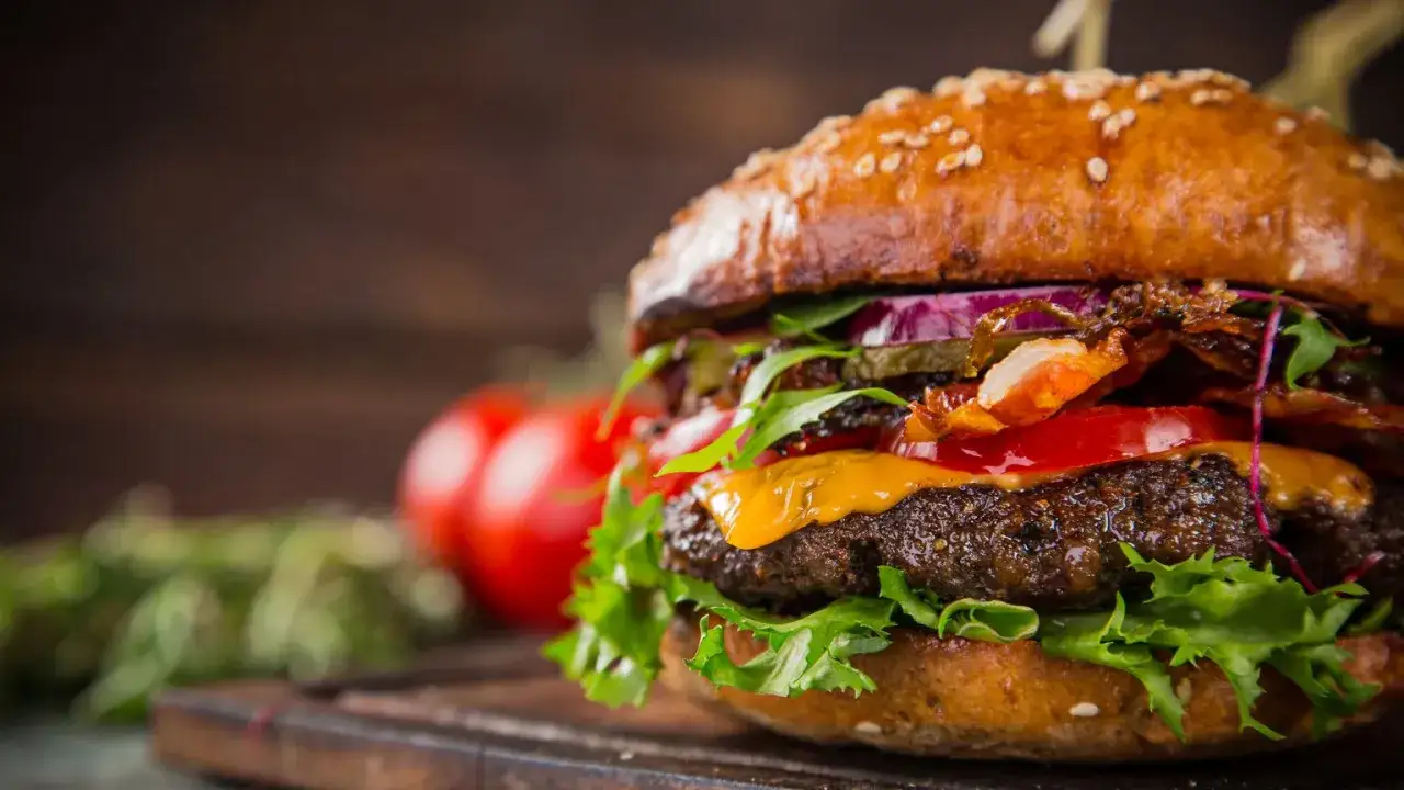 Soczysty burger z bekonem, serem i chrzanem, jak u drwala. Obok pomidory i zioła.