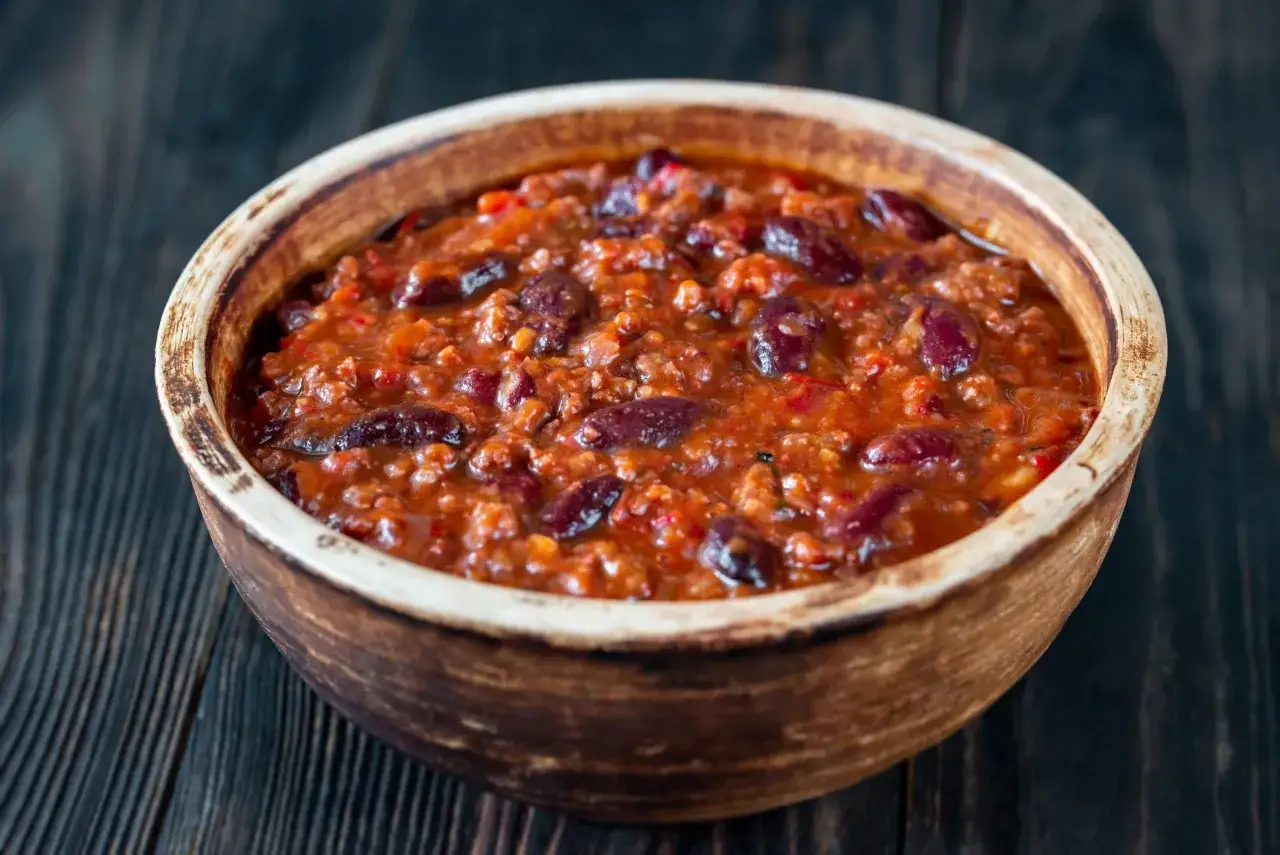 Miseczka pełna aromatycznego chili con carne przepis oryginalny, z fasolą i mielonym mięsem, na ciemnym drewnianym tle.