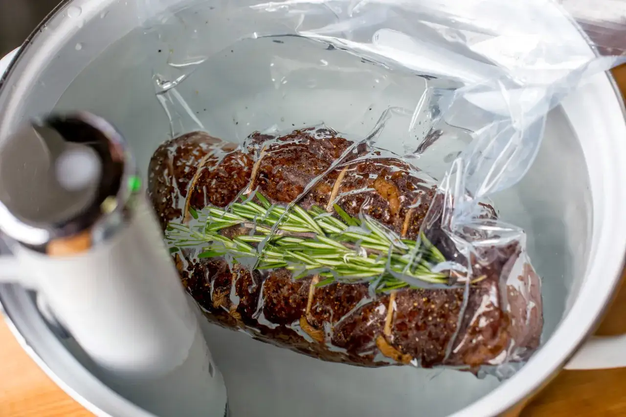 Mięso wołowe z rozmarynem w woreczku do gotowania sous vide, zanurzone w wodzie.