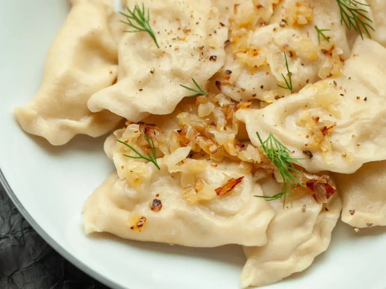 Pyszne pierogi ukraińskie z cebulką i koperkiem, posypane pieprzem, kuszą swoim wyglądem.