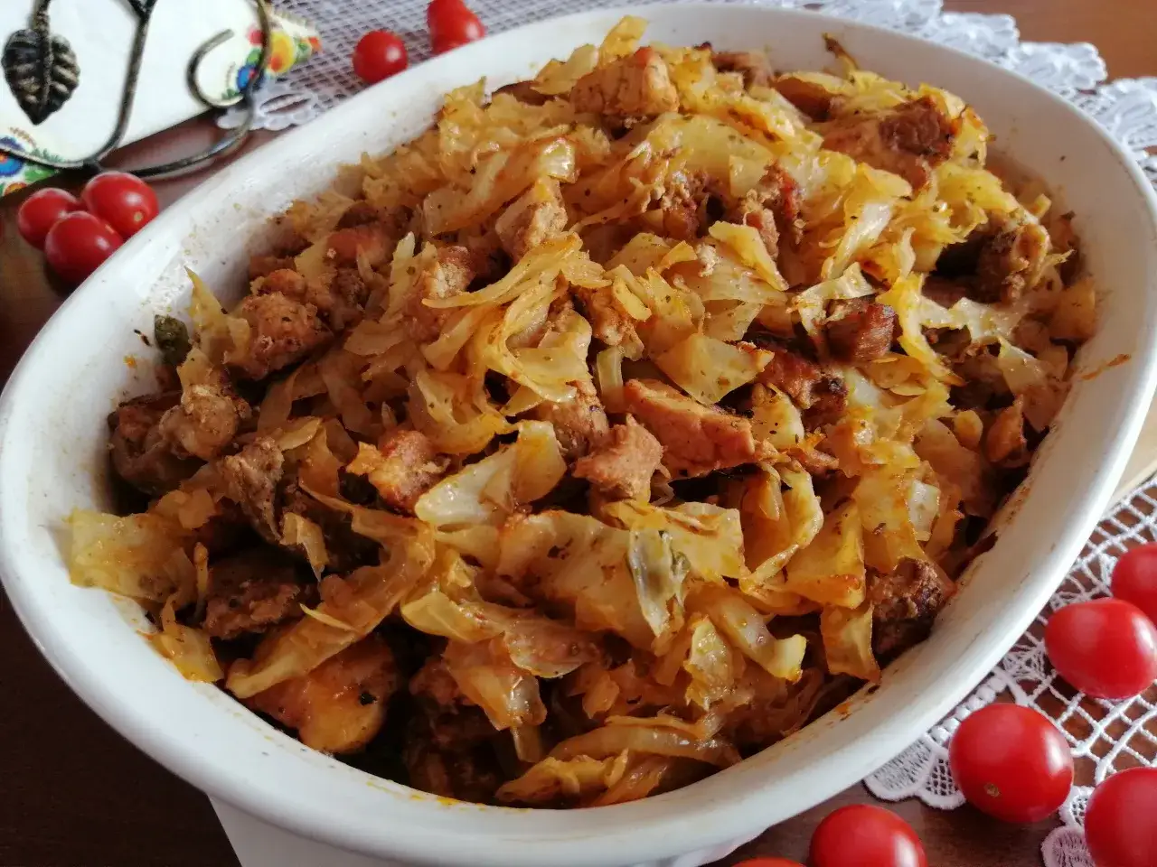Pyszna kapama z mięsem i kapustą, podana w białej zapiekance, ozdobiona pomidorkami koktajlowymi.