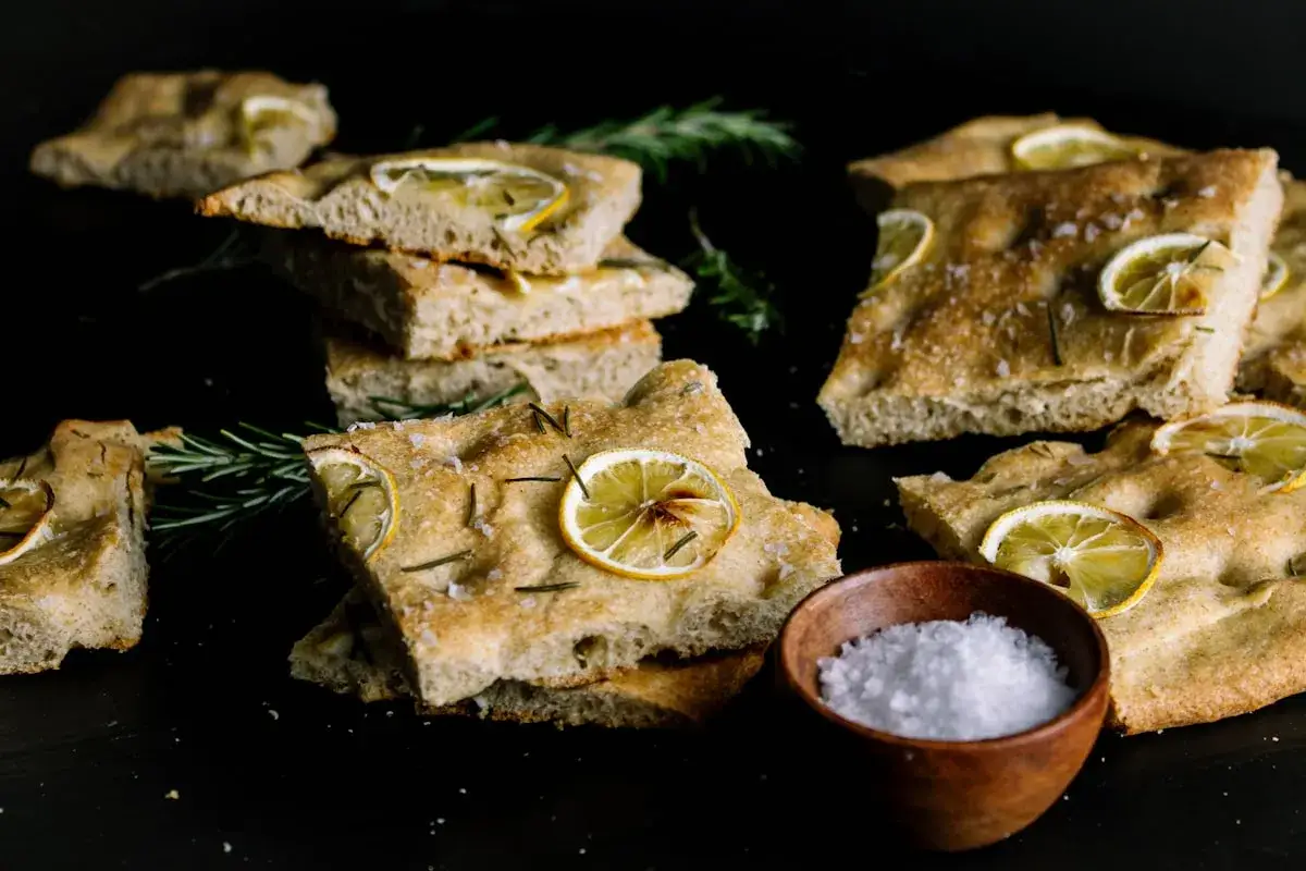 Oryginalna włoska focaccia przepis: chrupiące kromki z plasterkami cytryny i rozmarynem, obok miseczka soli.